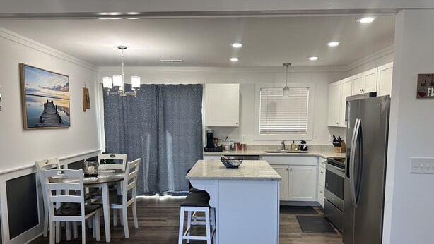 A modern kitchen with white cabinetry, a stainless steel refrigerator, and a dining area with white chairs and a table. - Cozy family retreat with great parking for multiple boats and vehicles! (Guntersville)