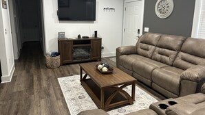 A living room with a brown leather sofa, a wooden coffee table, a flat-screen TV, and a fireplace. - Cozy family retreat with great parking for multiple boats and vehicles! (Guntersville)