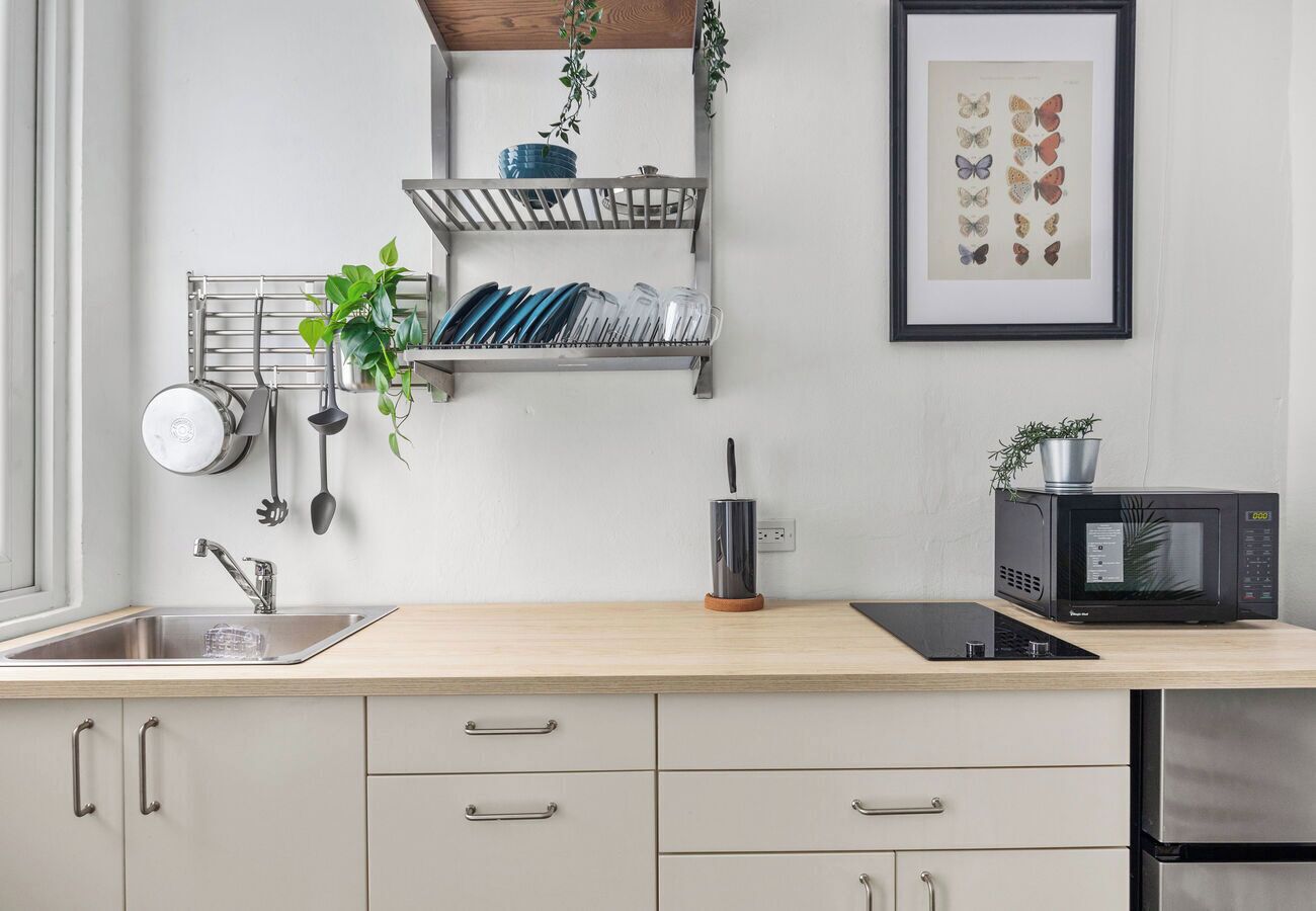 Una cocina moderna con un lavamanos, estufa y microondas. Hay armarios, una planta y un cuadro con una mariposa en la pared.