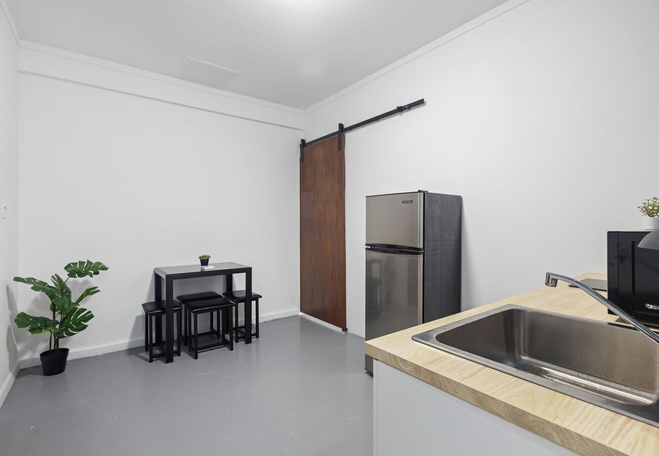 Une cuisine compacte comprenant un évier, un réfrigérateur, un meuble en bois, une petite table à manger avec des chaises et une plante en pot.