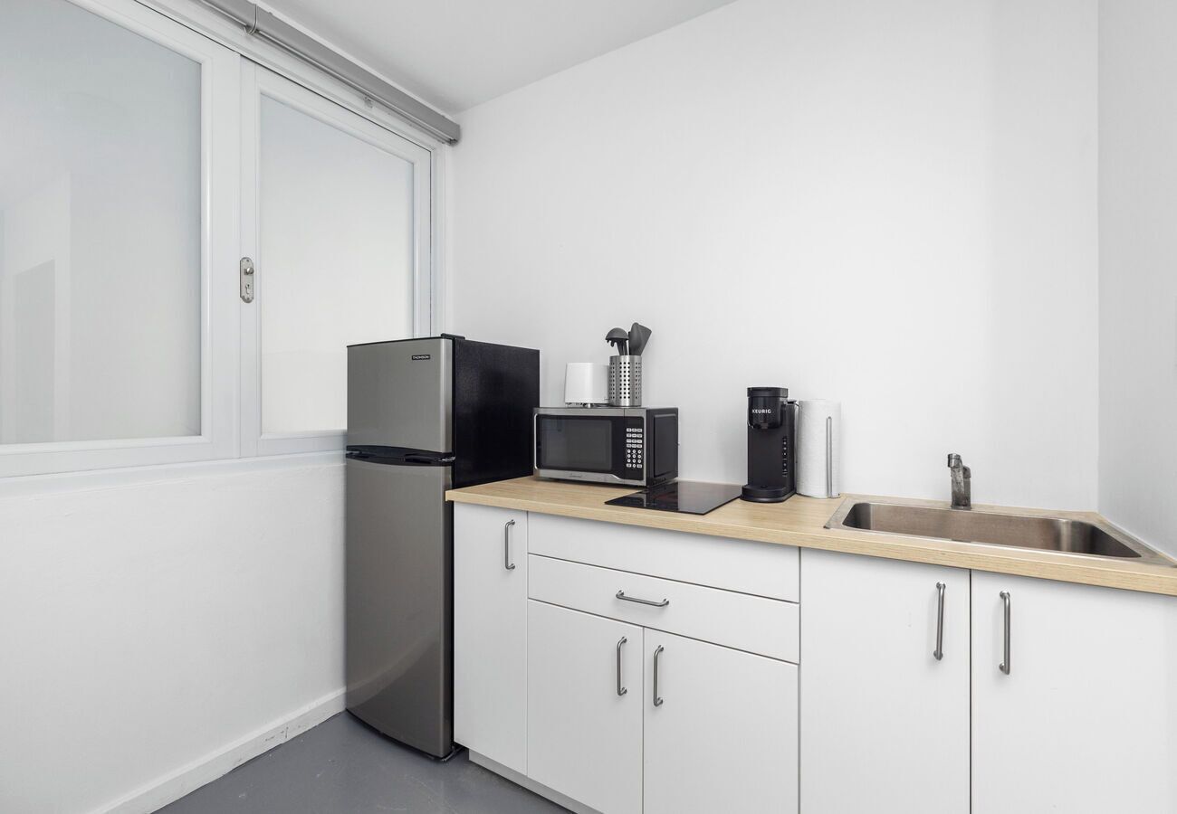 A compact kitchen with a stainless steel refrigerator, a microwave, a coffee maker, and a sink with a faucet.