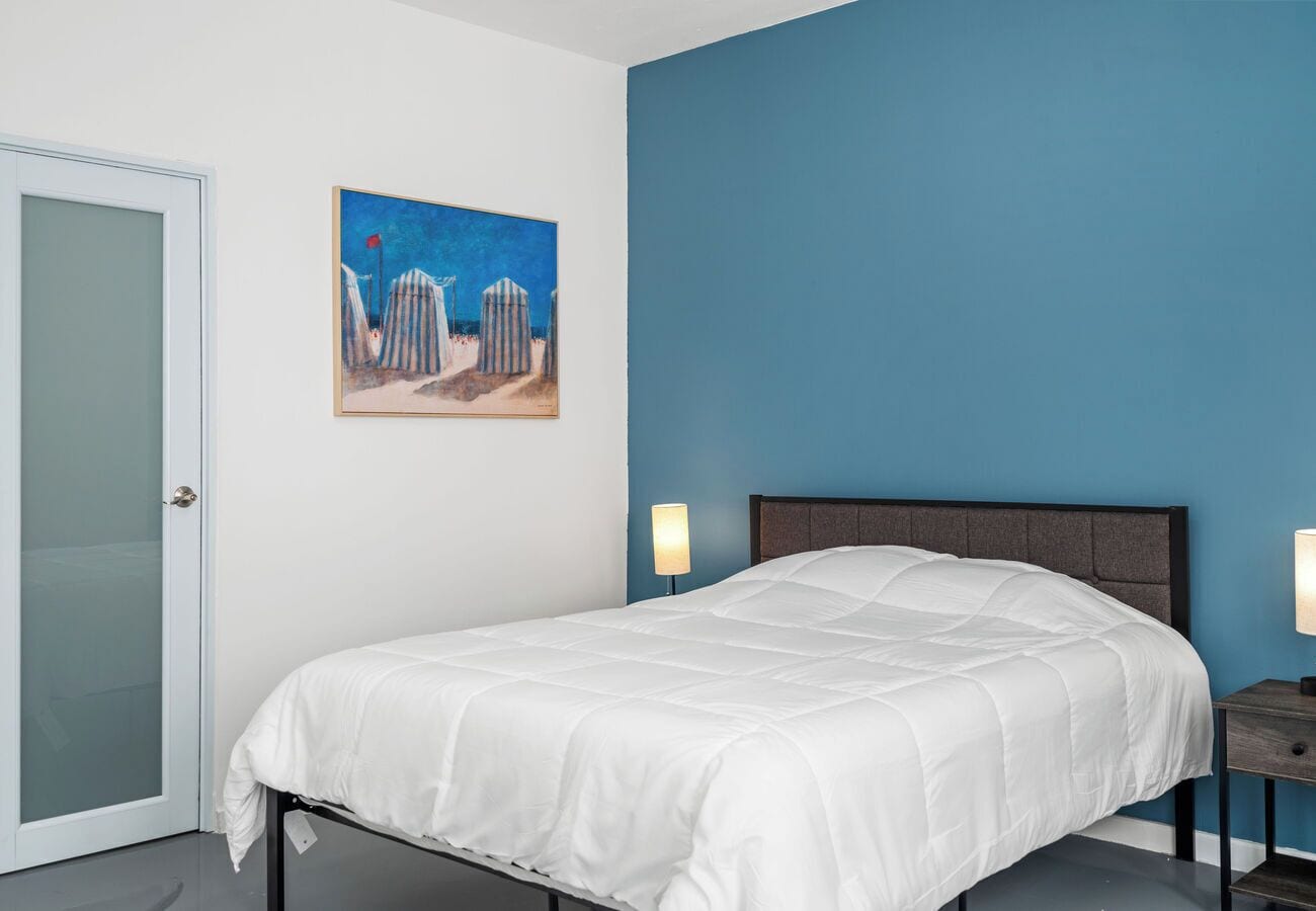 Un dormitorio con una cama, un cuadro, una mesita de noche y una puerta.