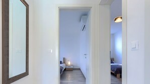 A narrow hallway leading to a bedroom with a bed, bedside table, and a lamp.