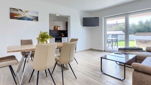 A modern living room with a dining area, a kitchen, and a large sliding glass door to the outdoors.