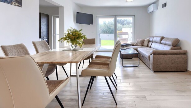 A modern living room with a dining area, a sofa, and a TV mounted on the wall.