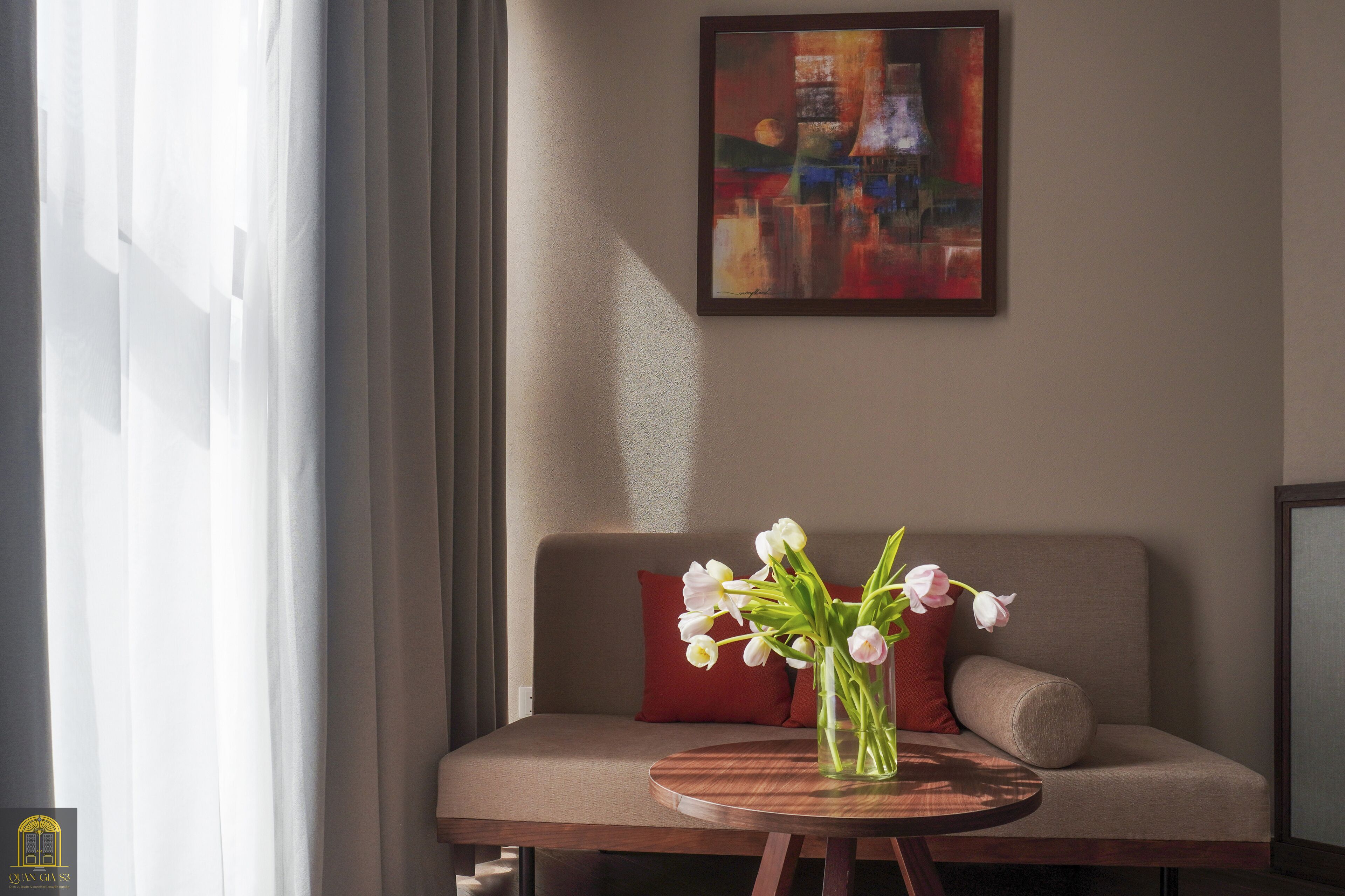 A room with a sofa, a round table with a vase of flowers, and a painting on the wall.