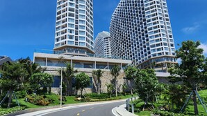 A modern high-rise building with a curved facade, surrounded by lush greenery and a clear blue sky. - Apec Mandala Beach Mui Ne Resort (Mui Ne)