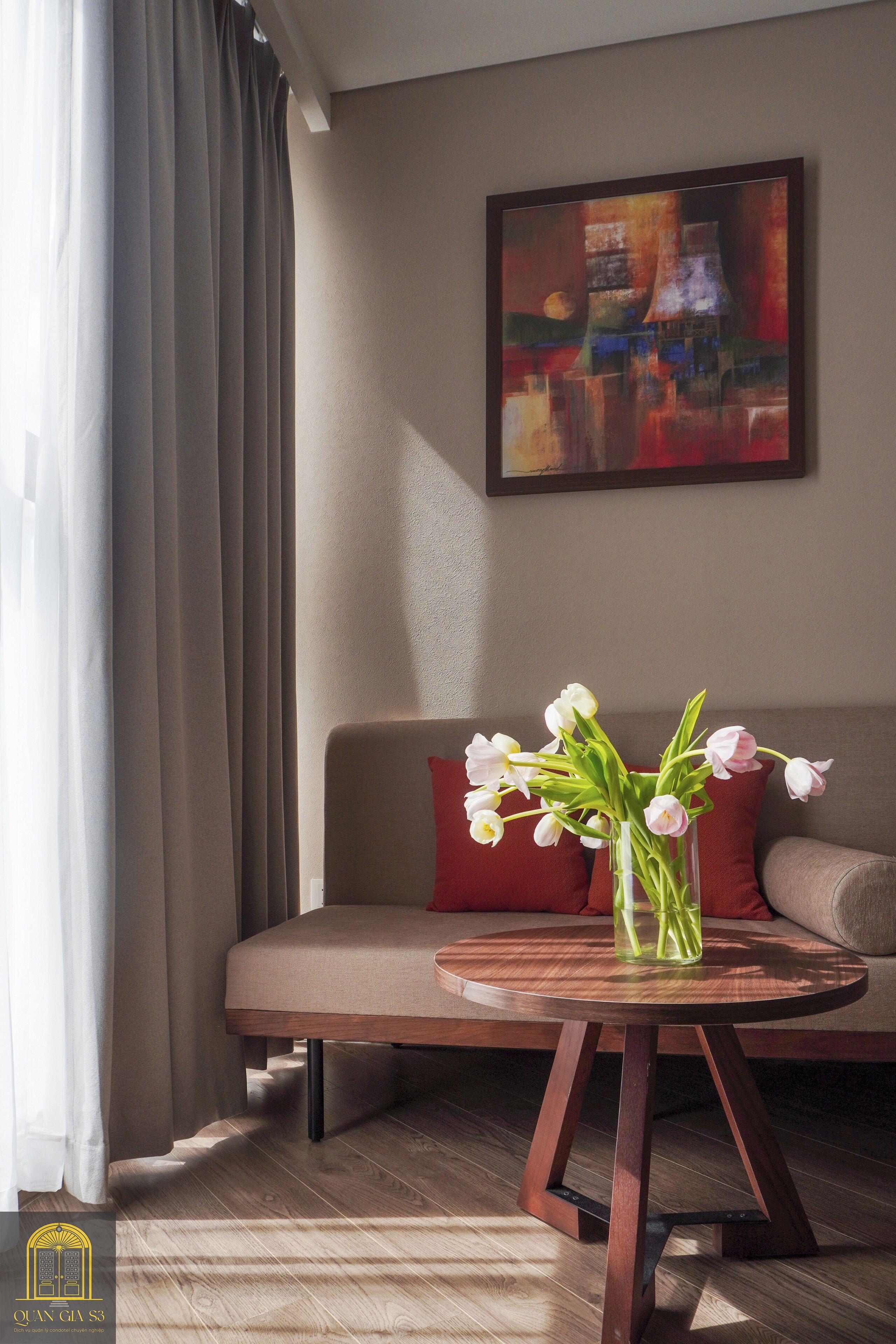 Un salon moderne avec un canapé, une table basse ronde en bois sur laquelle est posé un vase de fleurs, et un tableau accroché au mur.
