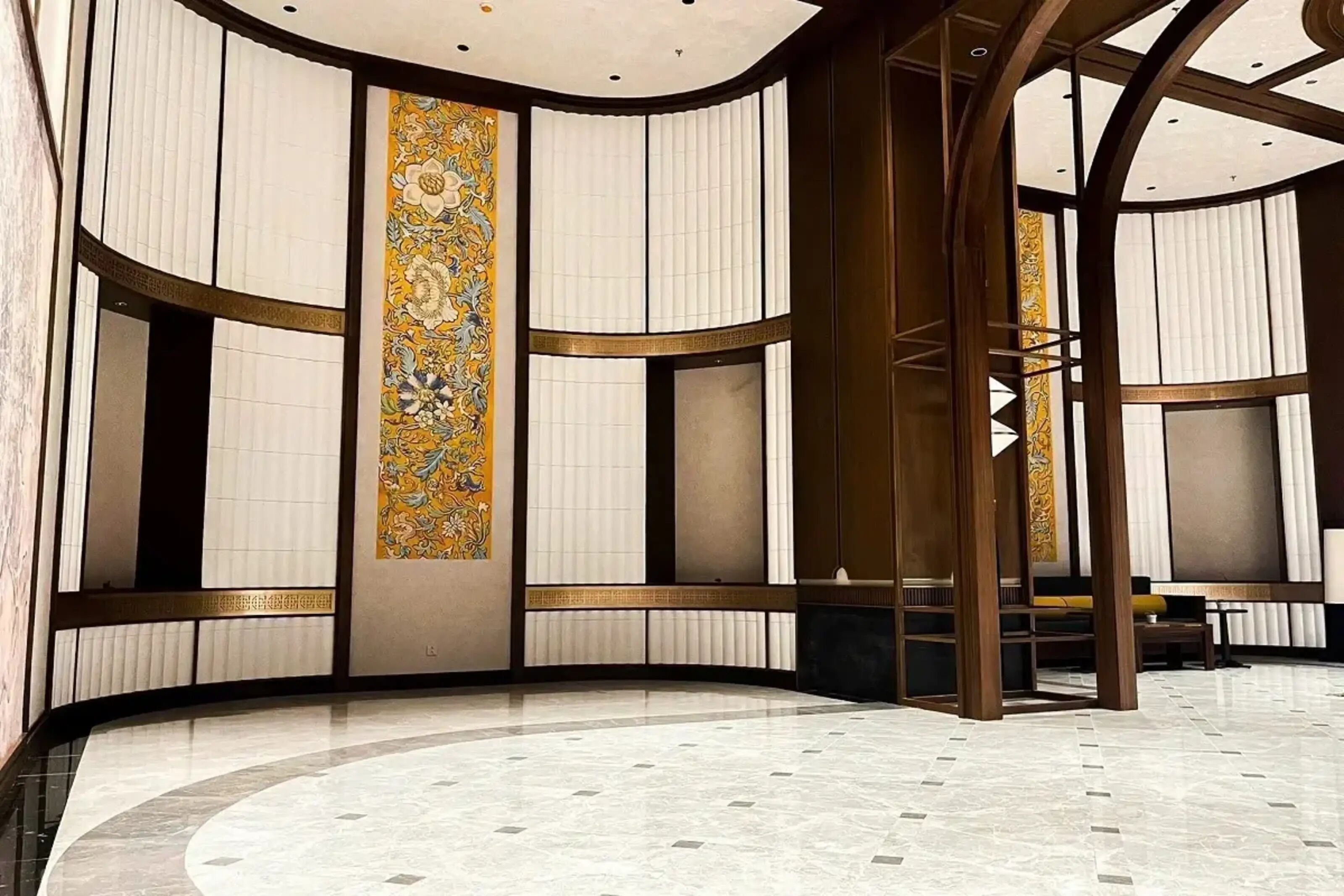 A spacious lobby with a curved marble floor, large windows with vertical blinds, and a decorative wall with a floral pattern.