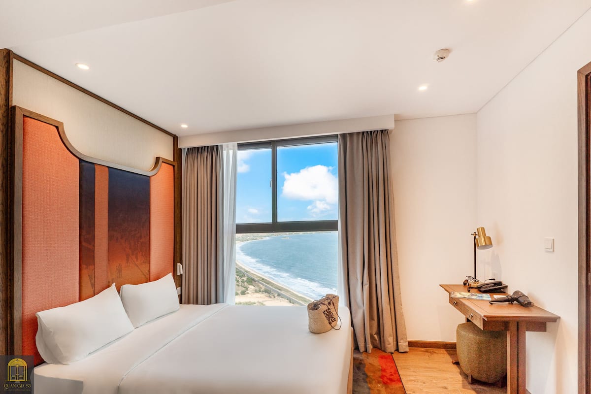 A hotel room with a large bed, a desk with a lamp, and a view of the ocean.