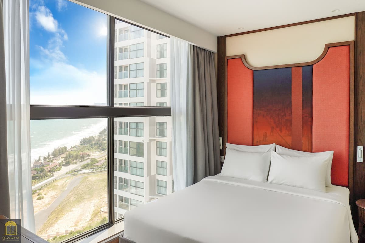 A hotel room with a large window offering a view of a building and a beach.
