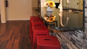 Una cocina con encimera de mármol, taburetes rojos, un fregadero y cuadros en la pared.