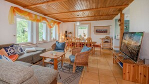 Un salon chaleureux avec un plafond en bois, un coin repas avec des chaises et une table, et un téléviseur posé sur un meuble en bois.