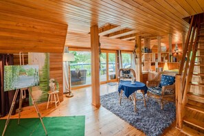 Ein Zimmer mit Holzwänden und -decke, einem Essbereich mit Tisch und Stühlen, einem Bücherregal und einem Bild an der Wand.