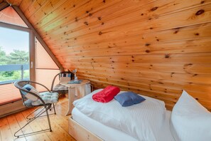 Une pièce chaleureuse avec un plafond en pente, un lit avec des oreillers, une chaise, une table et une vue par la fenêtre.
