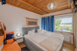 Un dormitorio con una cama grande, una mesita de noche, una lámpara, una ventana con cortinas y vistas al exterior.