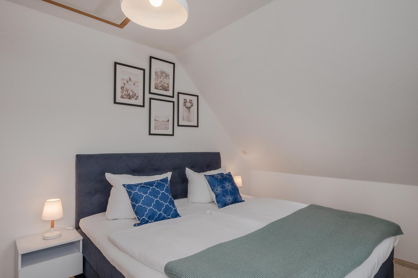 Un dormitorio con una cama, mesitas de noche, cabecera y cuadros en la pared.