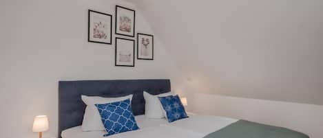 A bedroom with a bed, bedside tables, a headboard, and wall-mounted pictures.