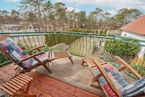 Un balcon agrémenté de deux fauteuils de jardin en bois, l’un avec un coussin à rayures et l’autre avec un coussin à carreaux.