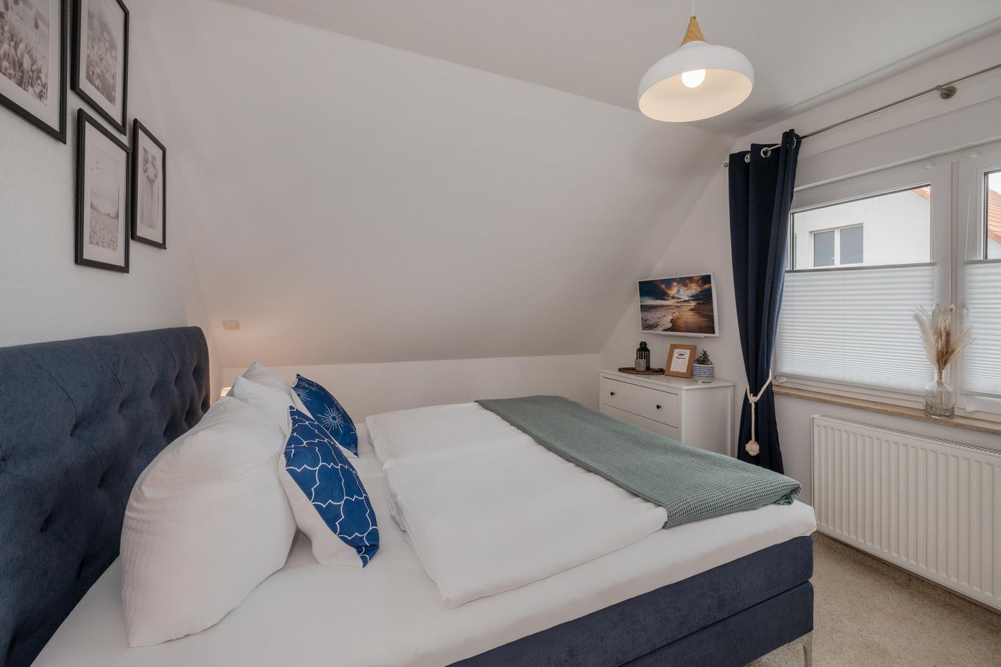 Quarto com cama, mesa de cabeceira e janela com cortinas.