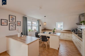 A modern kitchen with wooden flooring, a central island, and a dining area with chairs. - Ferienwohnung Strandlerche - Bequeme und Strandnahe Ferienwohnung für Max.5 Gäste im Seebad Ahlbeck (Heringsdorf)