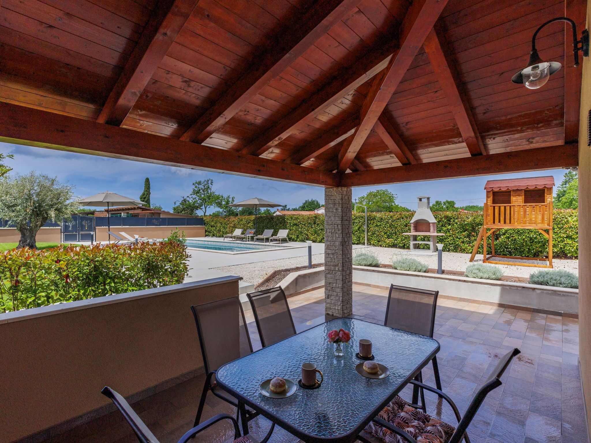 Alpendre coberto com mesa posta para dois, mobiliário para área externa e vista para uma piscina e jardim.