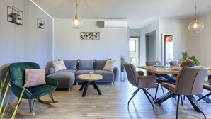 Ein modernes Wohnzimmer mit einem grauen Sofa, einem Schaukelstuhl, einem Esstisch mit Stühlen und Pendelleuchten.
