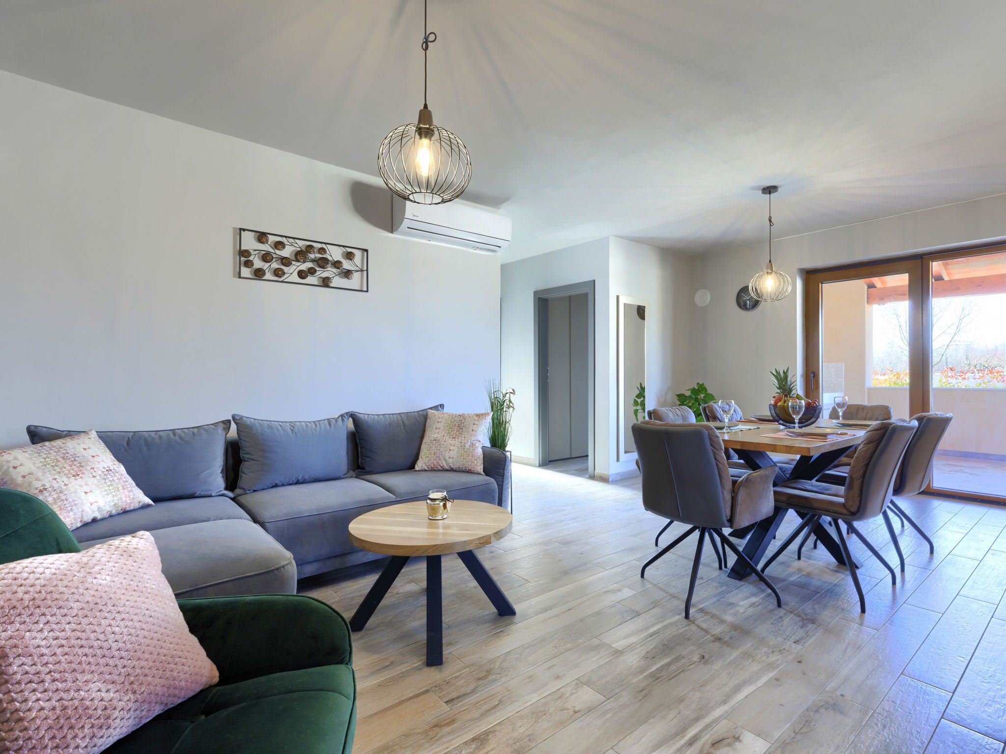 Un salon moderne avec un canapé gris, un fauteuil vert, une table basse en bois et un coin repas comprenant une table et des chaises.