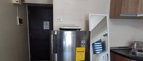 A compact kitchen with a stainless steel refrigerator, a microwave, and wooden cabinets.