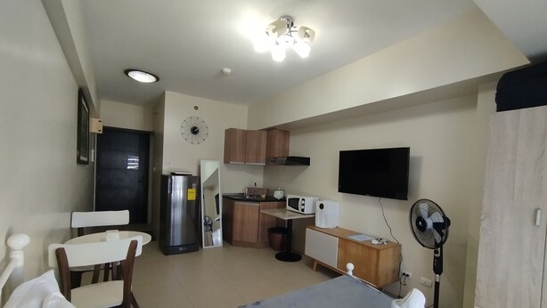 Una habitación de hotel compacta con una cama, un pequeño rincón de cocina, un televisor y un ventilador.