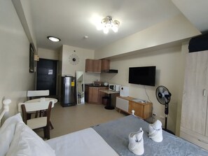 A compact hotel room with a bed, a small kitchenette, a TV, and a fan. - Cebu Avida Riala T1 1122 IT Park (Cebu City)