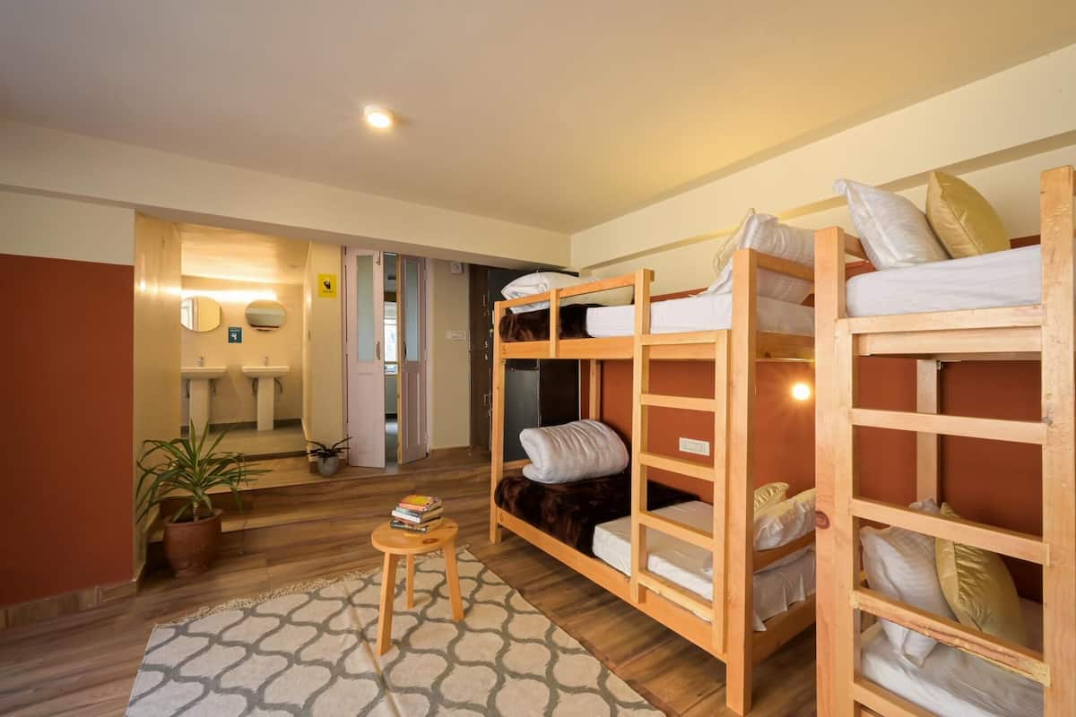 A room with bunk beds, a small table with books, a mirror, and a sink in the background.