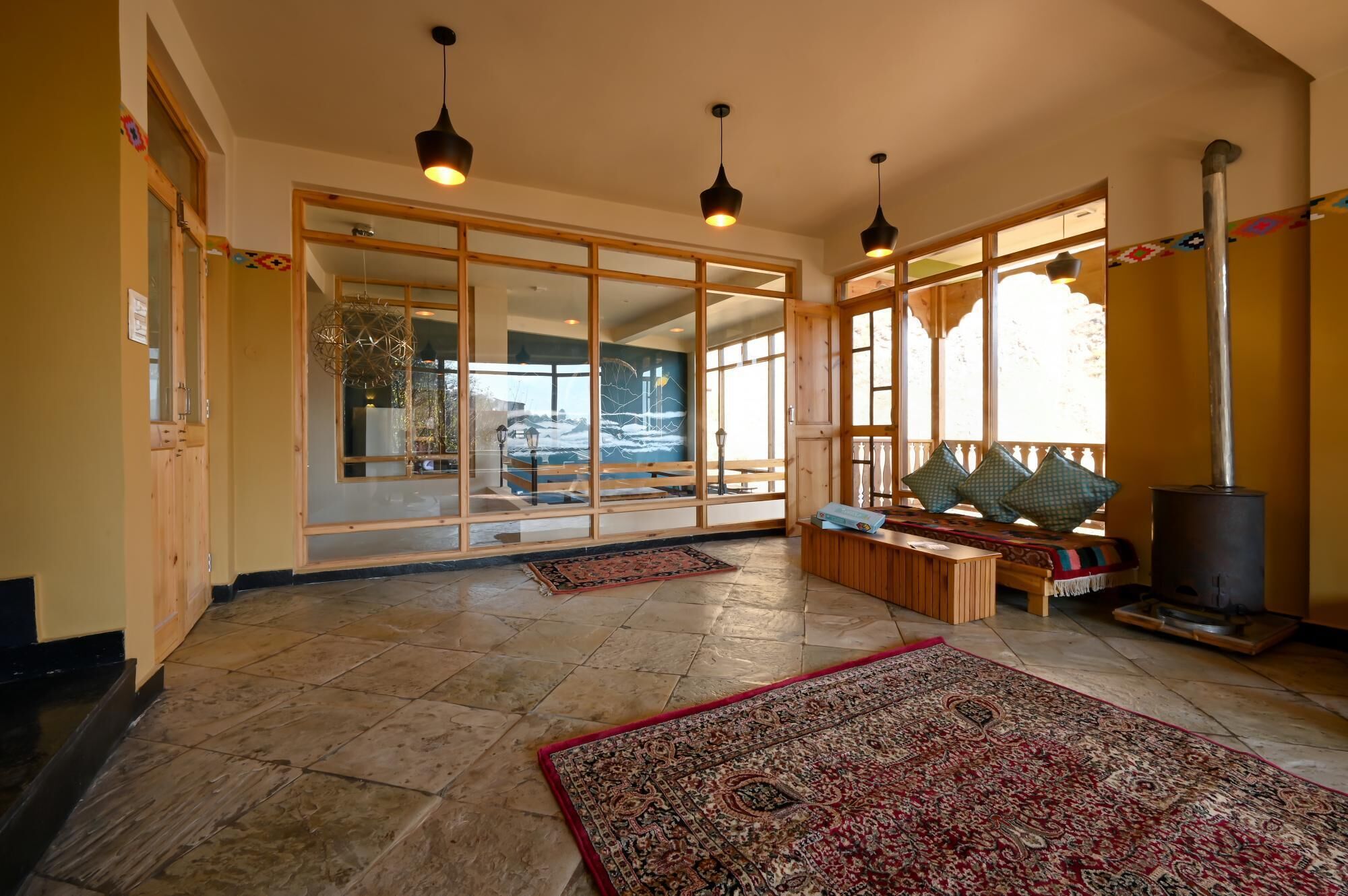 A spacious room with large windows, a stone floor, and a traditional rug.
