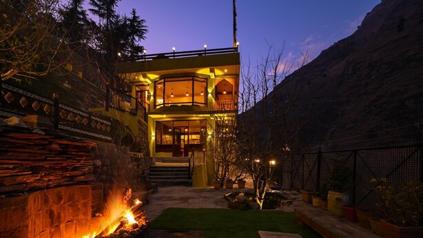 A modern house with a stone facade, a fire pit, and a well-maintained lawn. - Zostel Dobhi (Kullu)