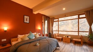 A bedroom with a large bed, two bedside tables, a chair, a small table, a potted plant, and a window with curtains. - Zostel Dobhi (Kullu)