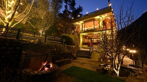 A two-story house with a stone facade, a fire pit, and a well-lit entrance. - Zostel Dobhi (Kullu)