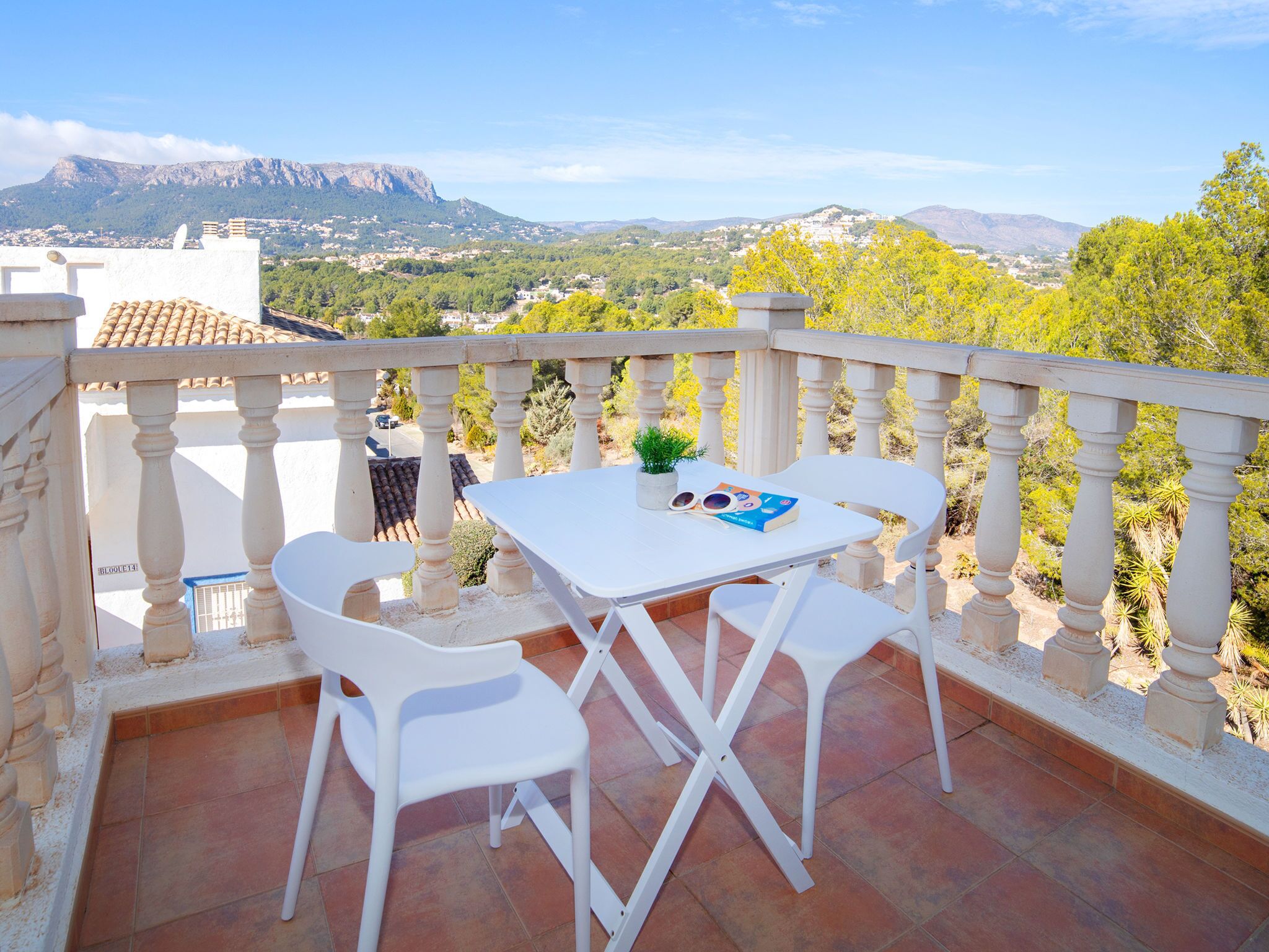 A terrace with a table and chairs, a potted plant, and a view of a mountainous landscape.