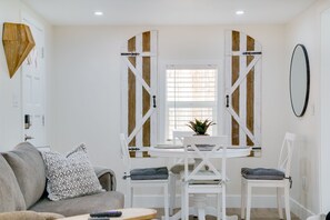 Een kamer met een witte eettafel, twee stoelen, een grijze bank en een houten deur met luiken.