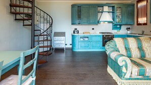A kitchen with teal cabinets, a stove, and a dining area with a chair and table.