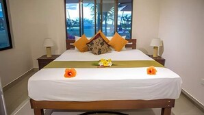 Una habitación de hotel con una cama grande, dos mesitas de noche y una ventana con vistas a palmeras.