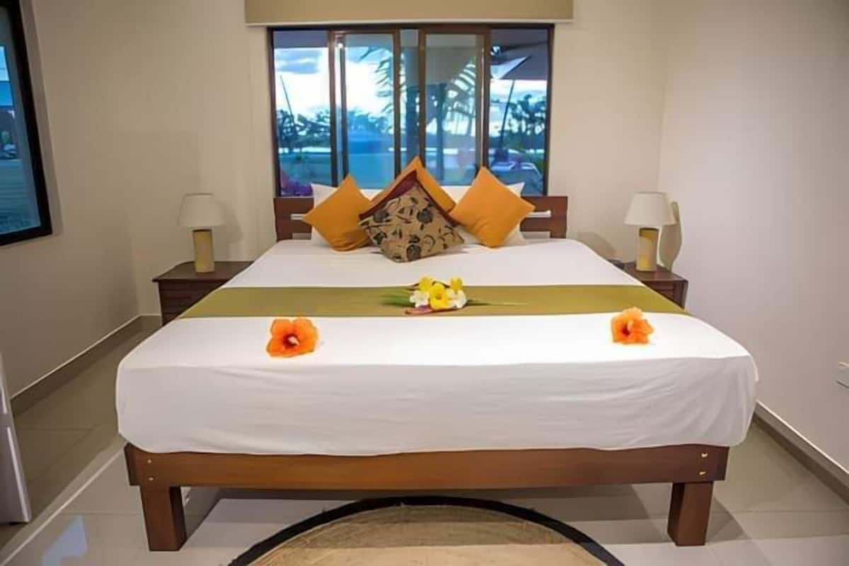 A hotel room with a large bed, two nightstands, and a window with a view of palm trees.