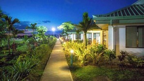 Un sendero bordeado de plantas que conduce a un edificio con techo verde y ventanas amplias.