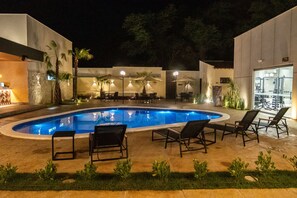 A swimming pool with lounge chairs and umbrellas, surrounded by a landscaped garden and a building with a glass door. - HOTEL SERRA DA CAPIVARA (São Raimundo Nonato)