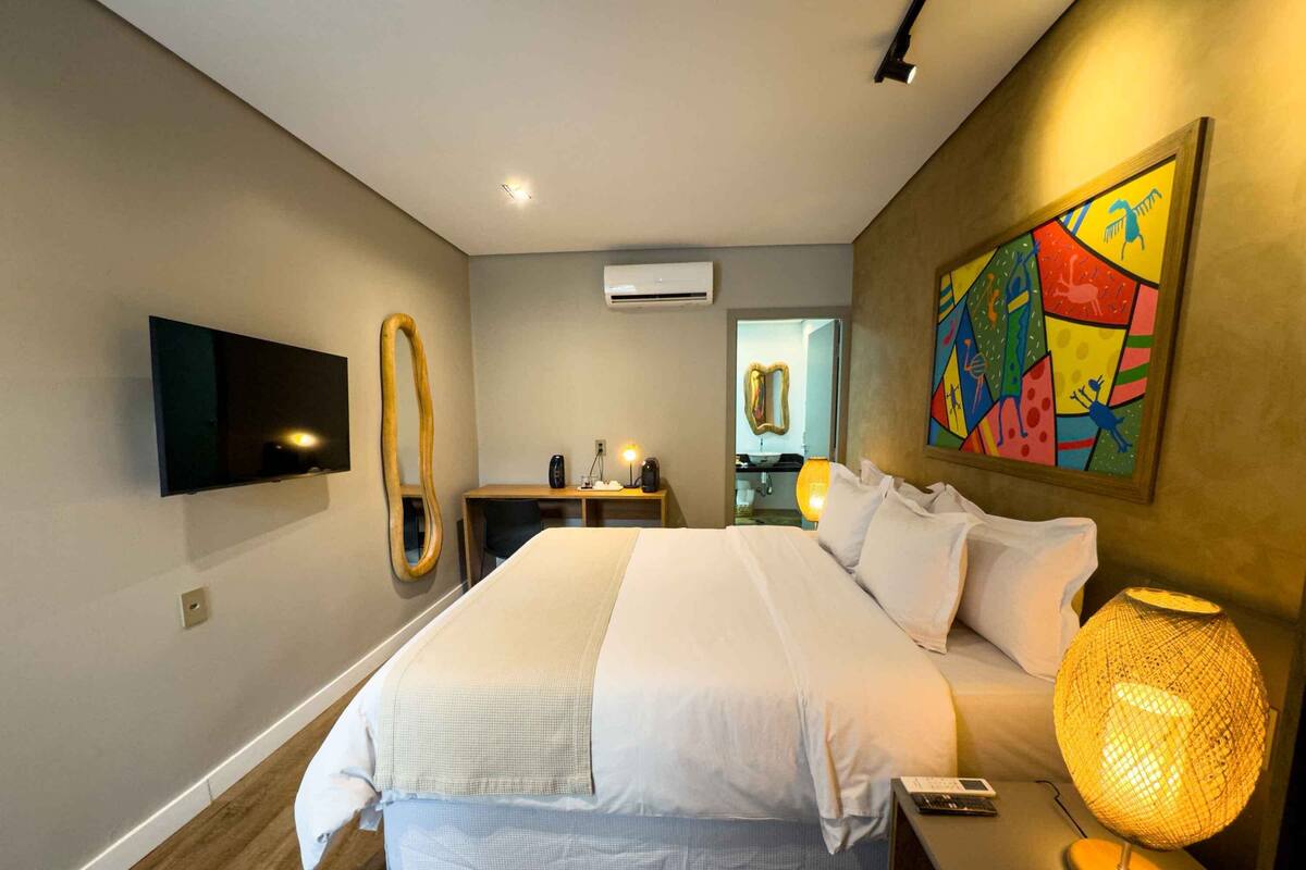 A modern hotel room with a large bed, bedside table, lamp, and a TV mounted on the wall.