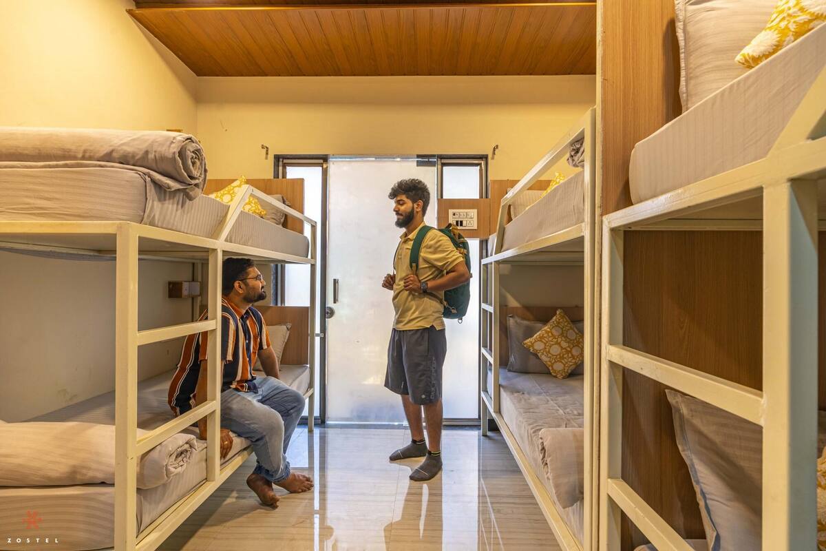 A dormitory room with bunk beds, a wooden ceiling, and a door leading to another room.