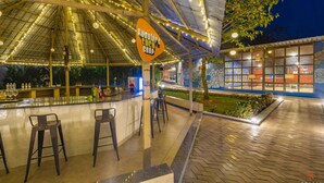 An outdoor bar area with a sign reading "Cuddler's Bar & Shop," featuring a counter with stools, a mural, and a view of the surrounding greenery. - Zostel Kolad (Roha)