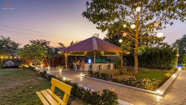 A gazebo with a tiled roof, surrounded by a garden with flowers and a bench. - Zostel Kolad (Roha)