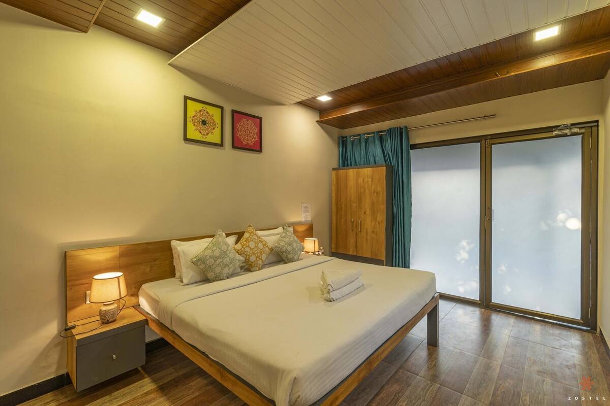 A bedroom with a wooden bed, nightstands, a large window with curtains, and two framed pictures on the wall.