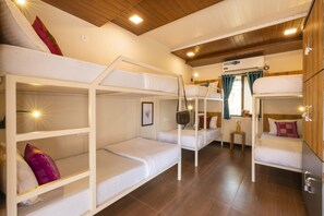 Une chambre avec un lit superposé, un plancher en bois, un ventilateur de plafond et une fenêtre avec des rideaux.