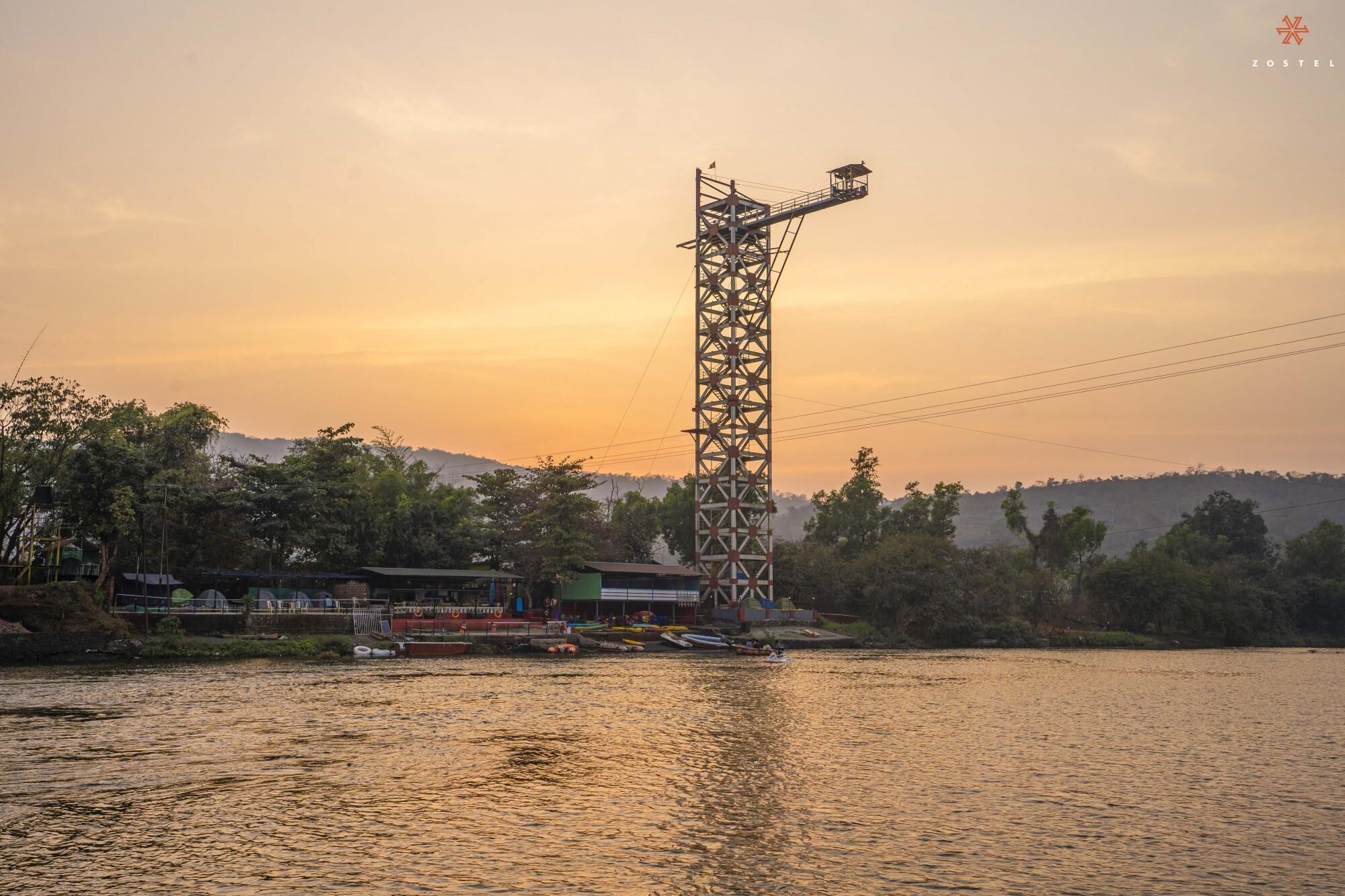 A tall metal structure by a river with boats and buildings in the background.